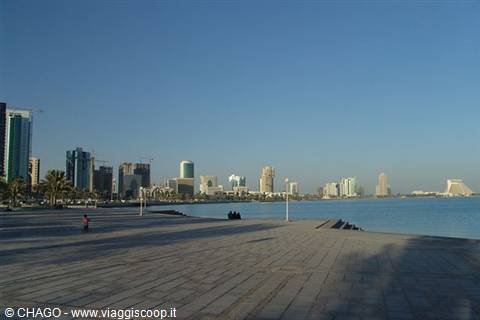 Doha Corniche: skyscrapers over the gulf, people sitting on the paved waterfront in the morning