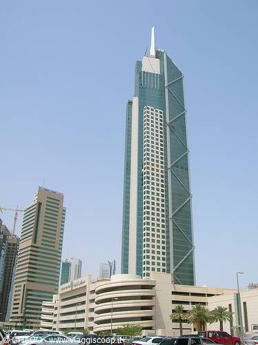 Glass and steel skyscraper in Kuwait City, blue sky, cars in foreground