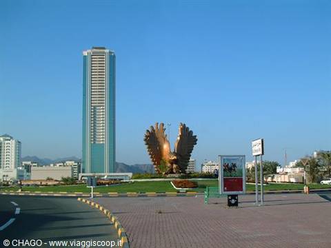 Golden falcon monument on a roundabout in front of a skyscraper in Fujairah