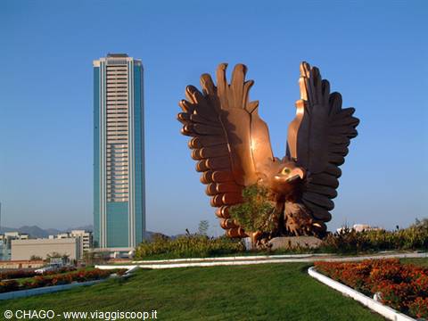 Golden eagle statue with spread wings in front of a skyscraper, Fujairah