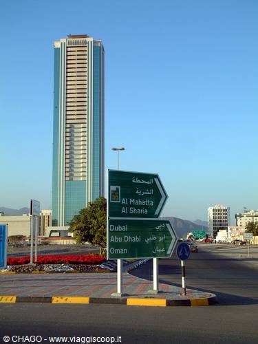 Road signs in Sharjah pointing to Dubai and Abu Dhabi, skyscraper behind