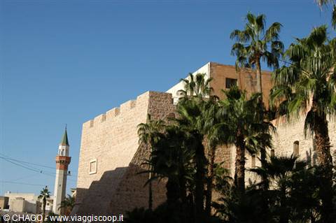 Stone walls of Tripoli's Red Castle among palms and a minaret