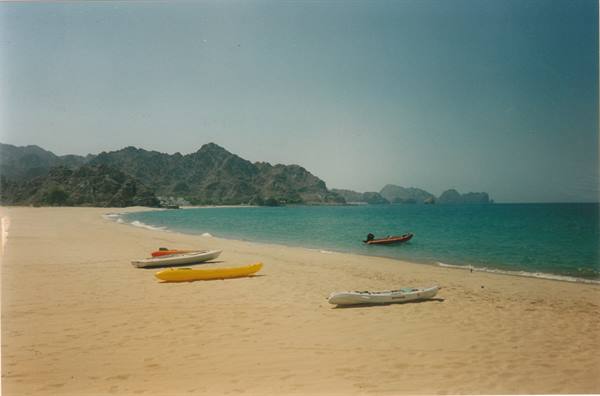 Yellow and white kayaks on the sand, turquoise sea and rocky mountains behind