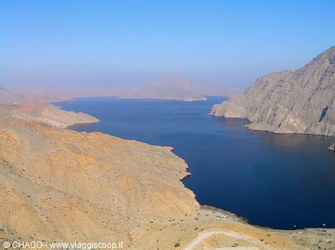 Dark blue inlet between arid rocky mountains under clear sky, Musandam