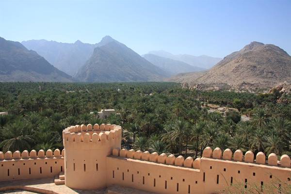 Crenellated adobe fort walls above a palm oasis and arid mountains