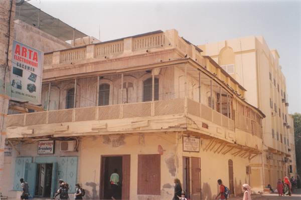 Colonial building with wooden balconies on the corner, people walk along the street