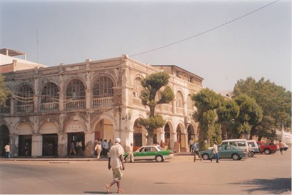 Colonial building with arches and arcades, pedestrians and cars on sunny street
