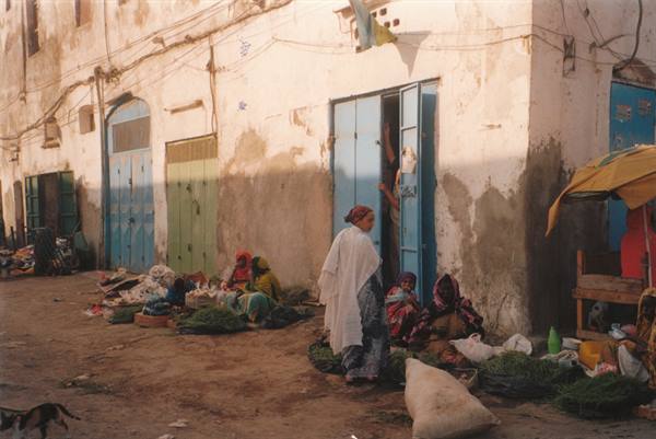 Women with vegetable sacks in front of blue doors on a dirt street