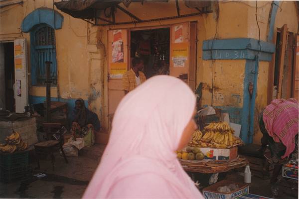 Woman in pink veil passing a street fruit stall with bananas