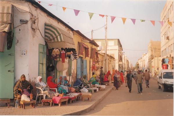 Veiled women selling fabrics under festive flags on a sandy street