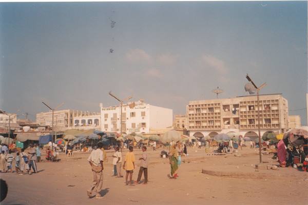 Children playing on sandy square in front of white buildings and market umbrellas