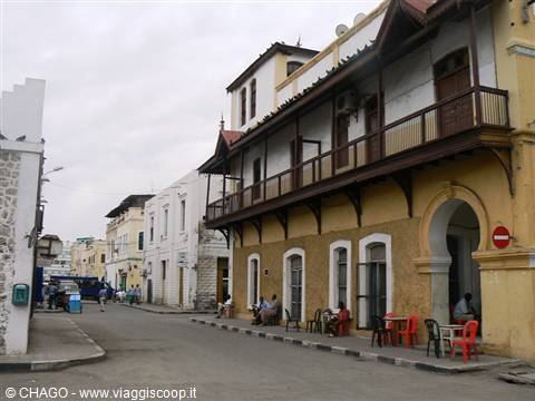 Stone Town street with yellow colonial building, wooden balconies and plastic chairs