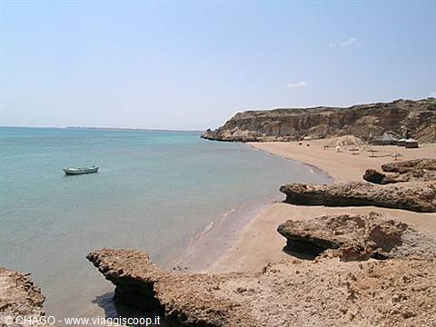 White boat floats on turquoise water beside rocky cliffs and sand