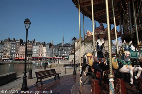Wooden horse carousel at Honfleur harbor with old waterfront houses behind
