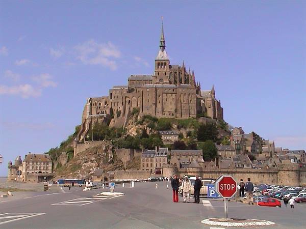 Tourists at the crosswalk in front of Mont-Saint-Michel abbey under blue sky