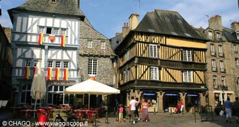 Half-timbered houses on Dinan square, people strolling past café umbrellas