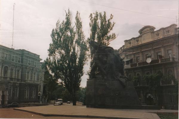 Stone monument with soldier figures among historic buildings and tall trees