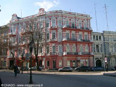 Pink and white Art Nouveau building in Odessa, cars parked under blue sky