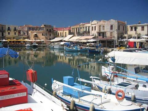 Fishing boats moored in Rethymno's Venetian harbour, colorful houses reflected in calm water