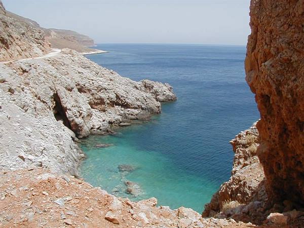 Reddish cliffs over turquoise water, dirt road along the coast