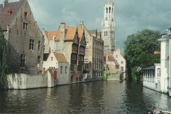 Bruges canal with brick houses and the medieval belfry tower under grey sky