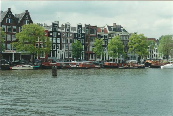 Amsterdam canal houses with houseboats moored along the Amstel under cloudy sky