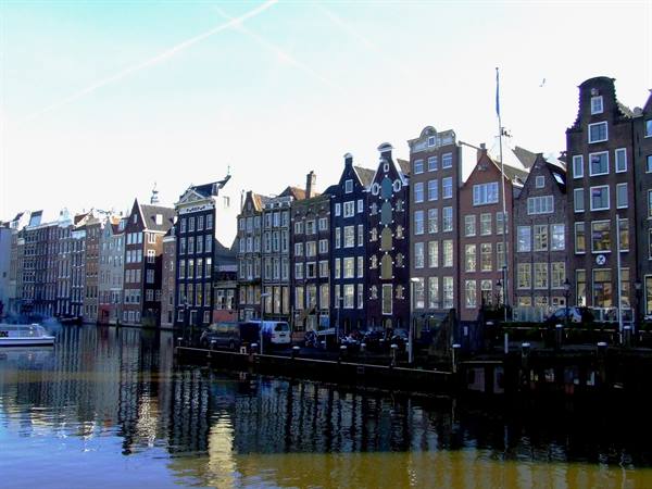 Traditional Dutch gabled houses along Amsterdam's Damrak canal, boat and reflections in the water