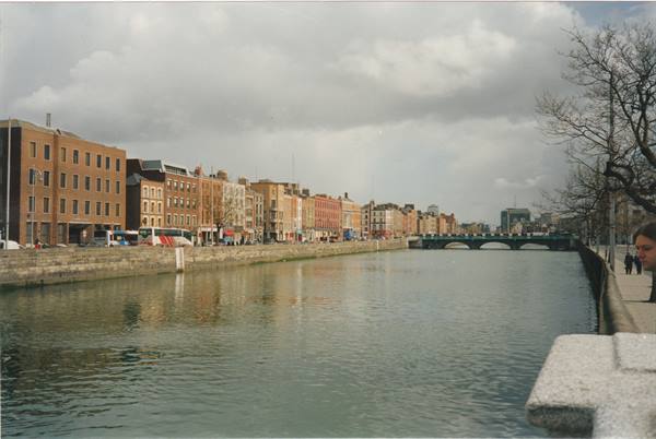 The River Liffey in Dublin between colorful buildings and a bridge under grey clouds