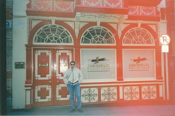 Man in white jacket outside solicitors' office with ornate red Victorian facade