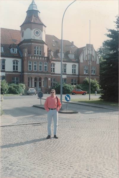 Man in pink shirt on cobblestones in front of historic brick building with turret