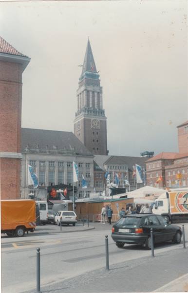 Kiel town hall square, brick tower with clock, flags, parked cars and trucks