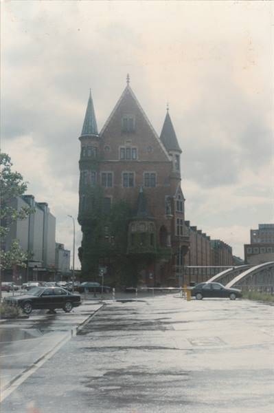 Red brick building with gothic towers, arched bridge and cars on wet street