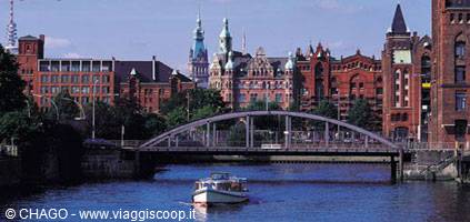 A boat passes under an iron bridge among red brick warehouses, Hamburg Speicherstadt