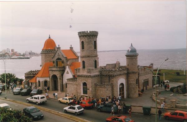 Stone castle with towers and orange roofs by the sea, tourists and cars