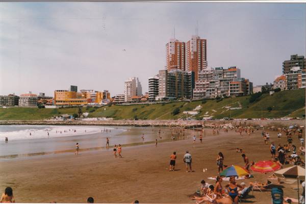 Beach with swimmers and colorful umbrellas, skyscrapers above green cliffs