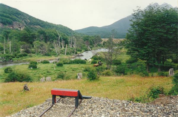 Red buffer stop at rail end, river and green meadows among mountains