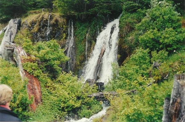 Waterfall cascading through mossy rocks and green forest, blonde person watching below