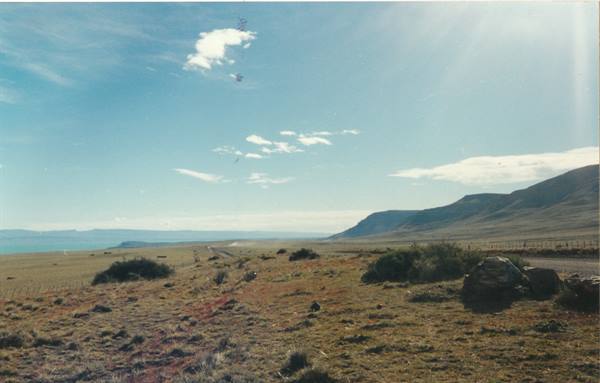 Road crossing grassy Patagonian steppe toward the blue lake under cloudy sky