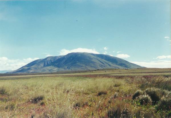 Green mountain rising over grassy plain, blue sky with scattered clouds