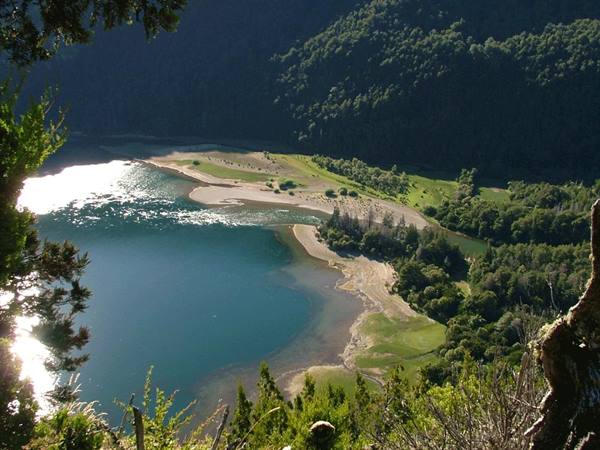 Turquoise lake surrounded by green forests and sandy sunlit beach