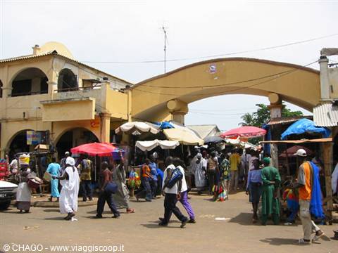 Busy market beneath a large yellow arch, colorful umbrellas and pedestrians