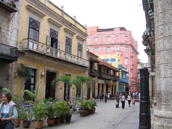 Pedestrians walking past colorful colonial buildings and potted palms in Havana