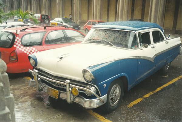 Vintage blue and white car parked in the rain next to a red taxi, Havana