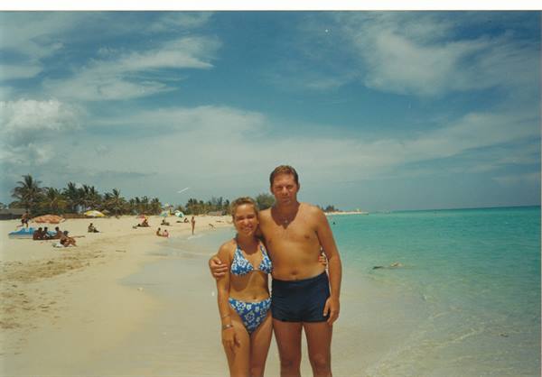 Couple in swimwear on white sand, palms and umbrellas, turquoise sea and clouds