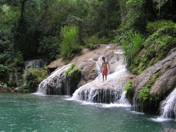 Boy in red swimsuit standing on limestone waterfalls surrounded by lush jungle