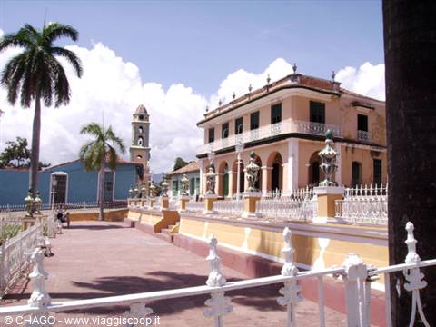 Plaza Mayor in Trinidad: yellow colonial building, palm tree and bell tower under white clouds