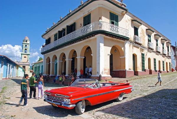 Red vintage convertible on cobblestones before colonial arched building, Trinidad
