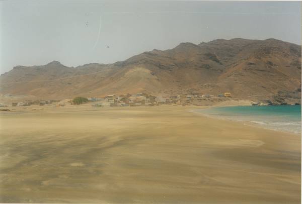 Low houses village between arid mountains and golden sand, turquoise sea