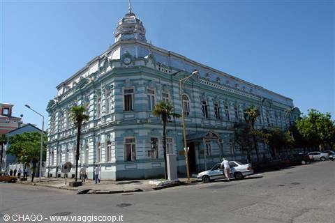 Historic pale blue wooden building with turret, street corner with palms and cars