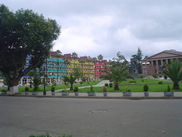 Palms and gardens in front of a hotel with multicolored balconies, cloudy sky
